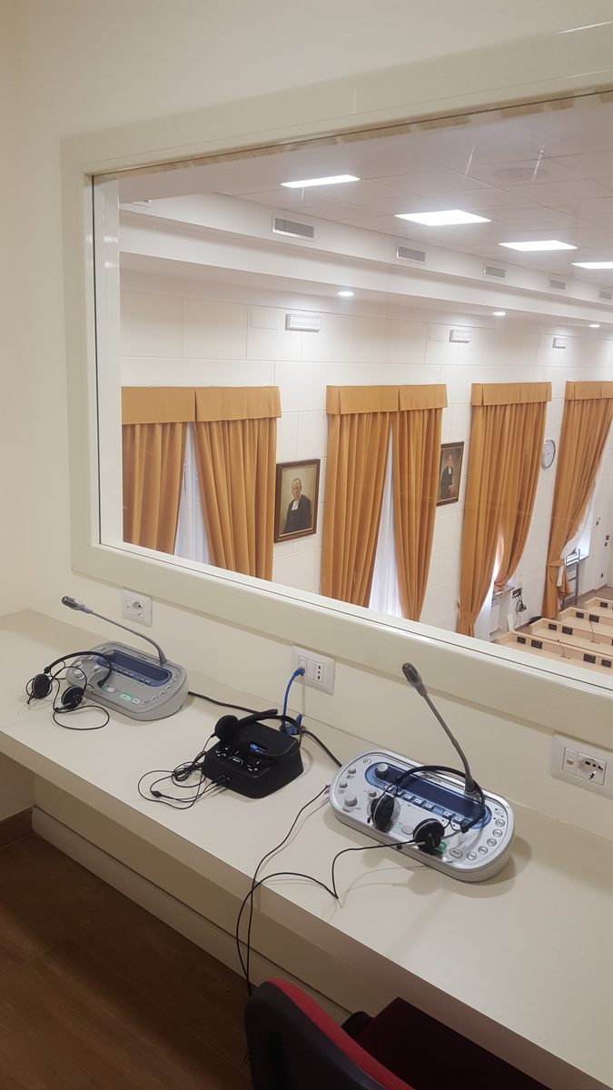 Cabina degli interpreti con consolle e cuffie, affacciata sulla sala attraverso il vetro